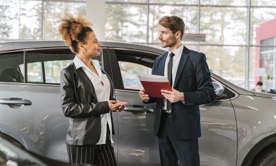 men and woman talking with folder and car behind