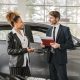men and woman talking with folder and car behind