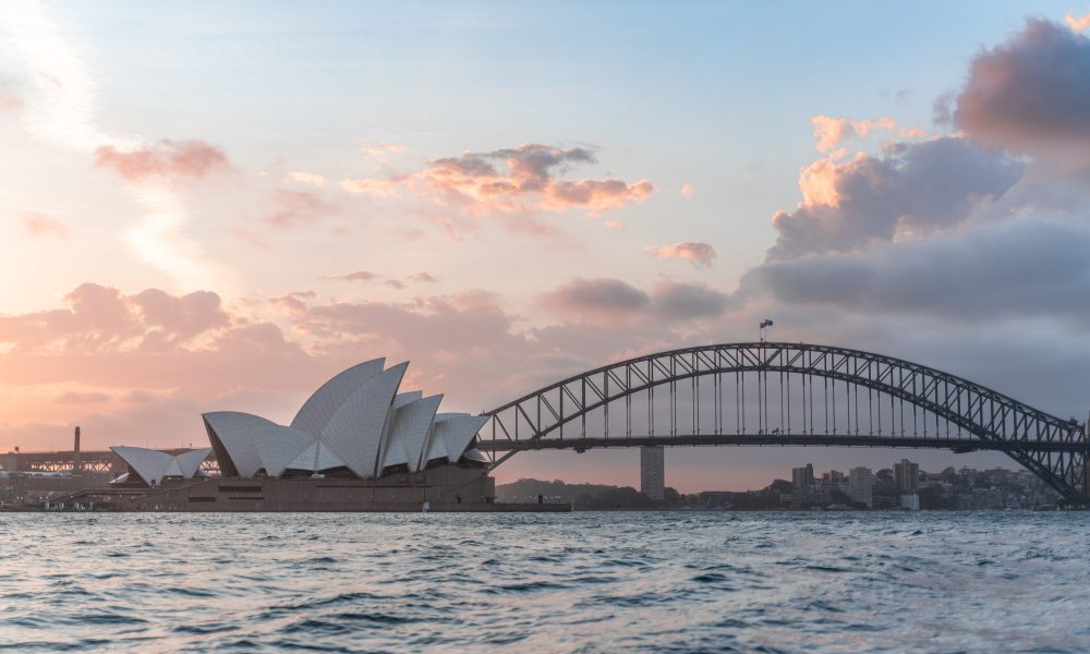 Stylish modern building and arch bridge crossing harbor against cloudy sundown sky