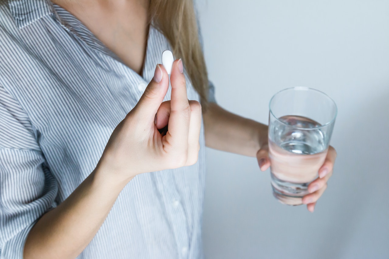 woman holding medicine pill and glass of water