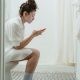 Woman Sitting on a Toilet and Using Phone