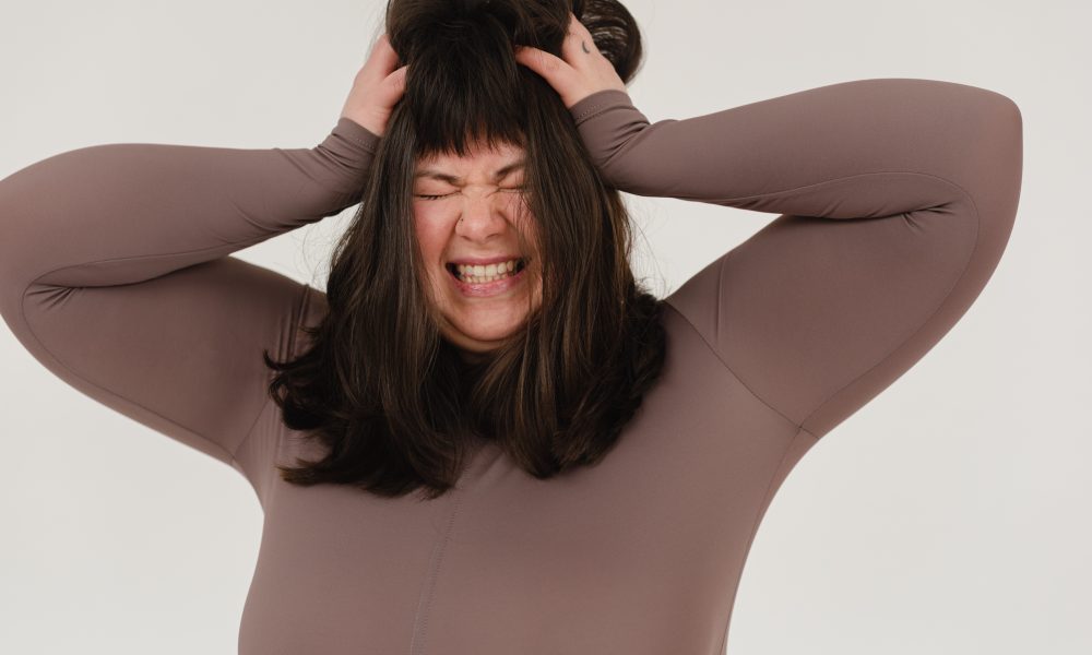 Young obese woman rumpling hair with closed eyes in white studio