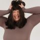 Young obese woman rumpling hair with closed eyes in white studio