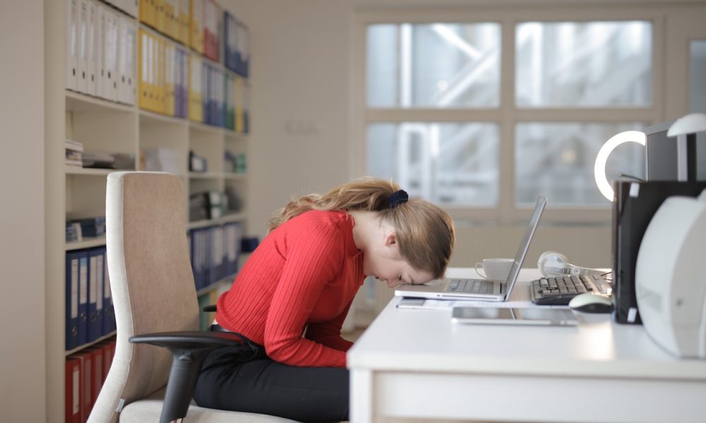 woman in red long sleeves with head leaning on laptop
