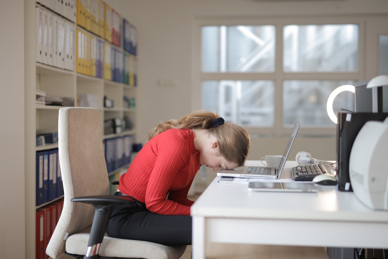 woman in red long sleeves with head leaning on laptop