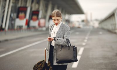 Worried young businesswoman with suitcase hurrying on flight on urban background