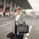 Worried young businesswoman with suitcase hurrying on flight on urban background