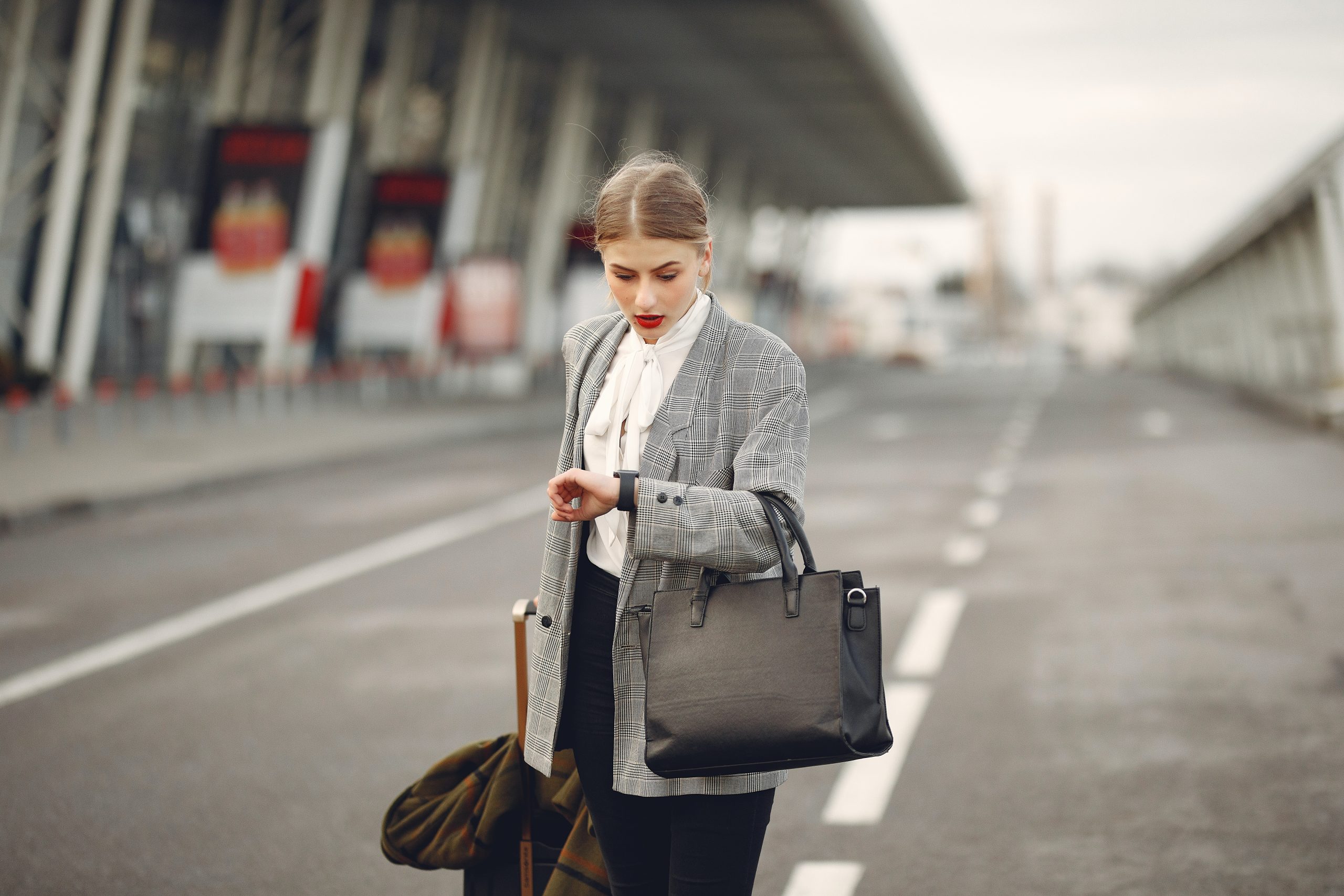 Worried young businesswoman with suitcase hurrying on flight on urban background