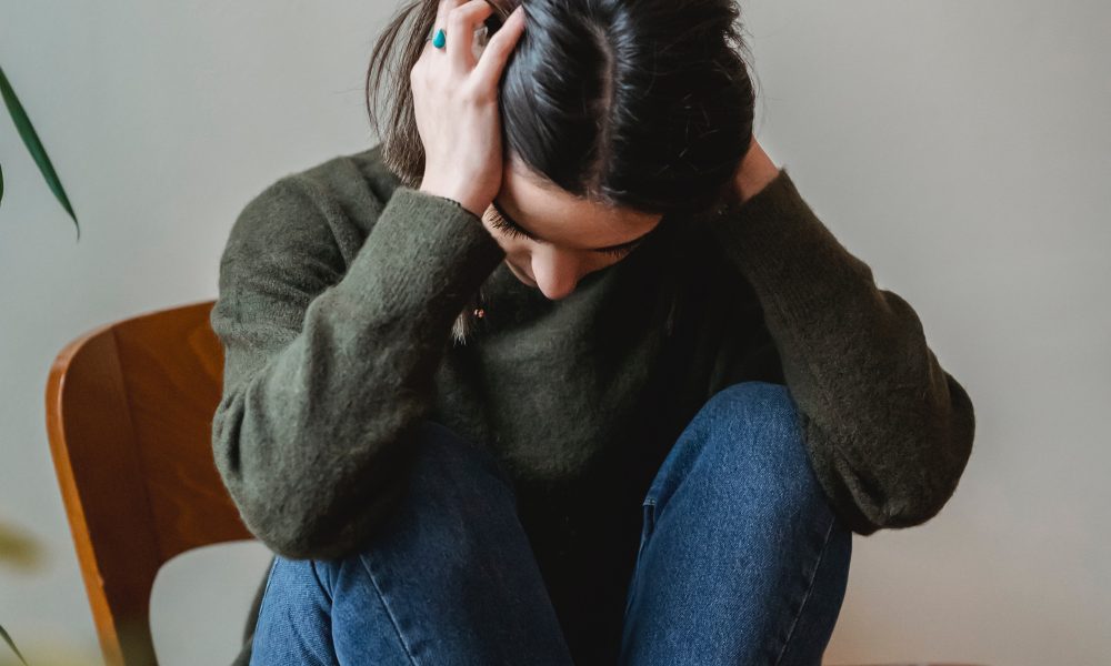 Anxious young woman cover wing ears with hands sitting on chair