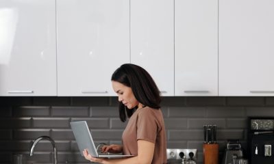 A Woman Working on Her Laptop while Standing Near Her Kids Eating Breakfast