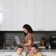 A Woman Working on Her Laptop while Standing Near Her Kids Eating Breakfast