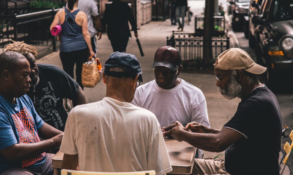 Men Sitting Beside Table on Pathway Near People Walking Beside Rail