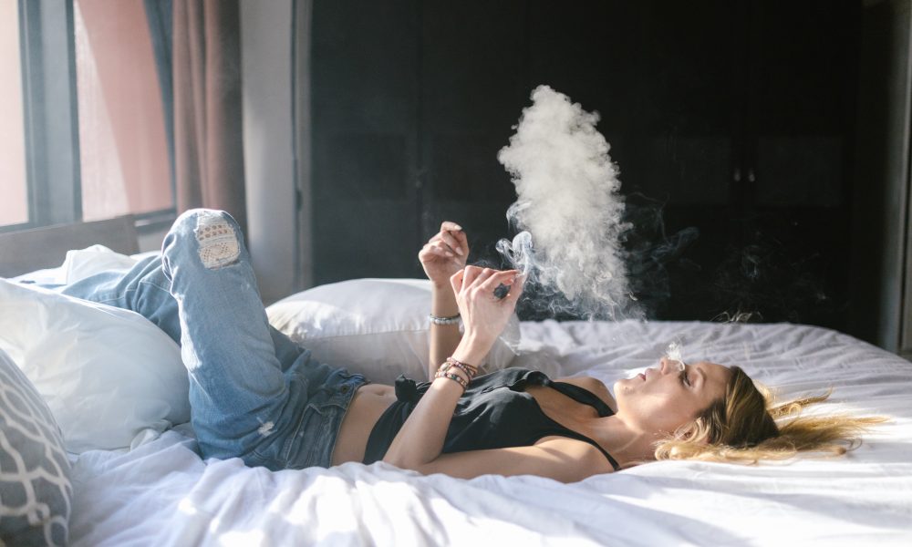 A Woman Wearing Tank Top and Denim Jeans Lying on the Bed While Smoking