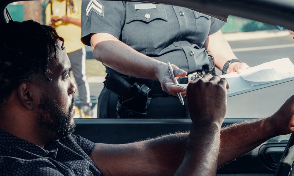 A Man Sitting Inside the Car Handing the License to the Police Officer