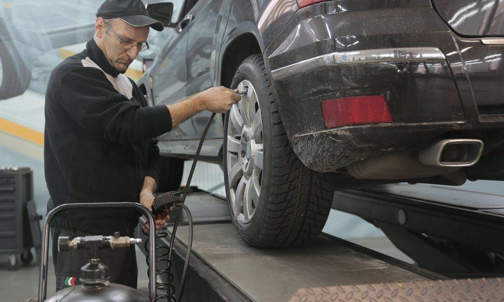 Serious car mechanic pumping up car wheel in modern service garage
