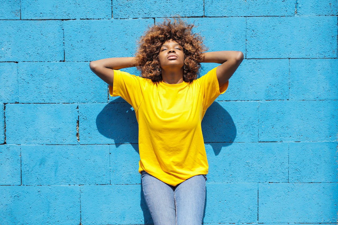 A Lady in Yellow Shirt Leaning Against Blue Brick Wall