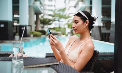 Young ethnic woman messaging on smartphone while chilling in cafe near outdoor pool