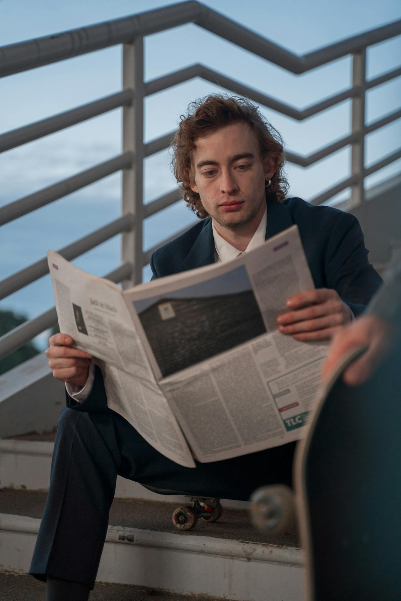 A Man Sitting on Staircase Reading a Newspaper