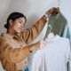 Happy young woman choosing pullovers on hangers