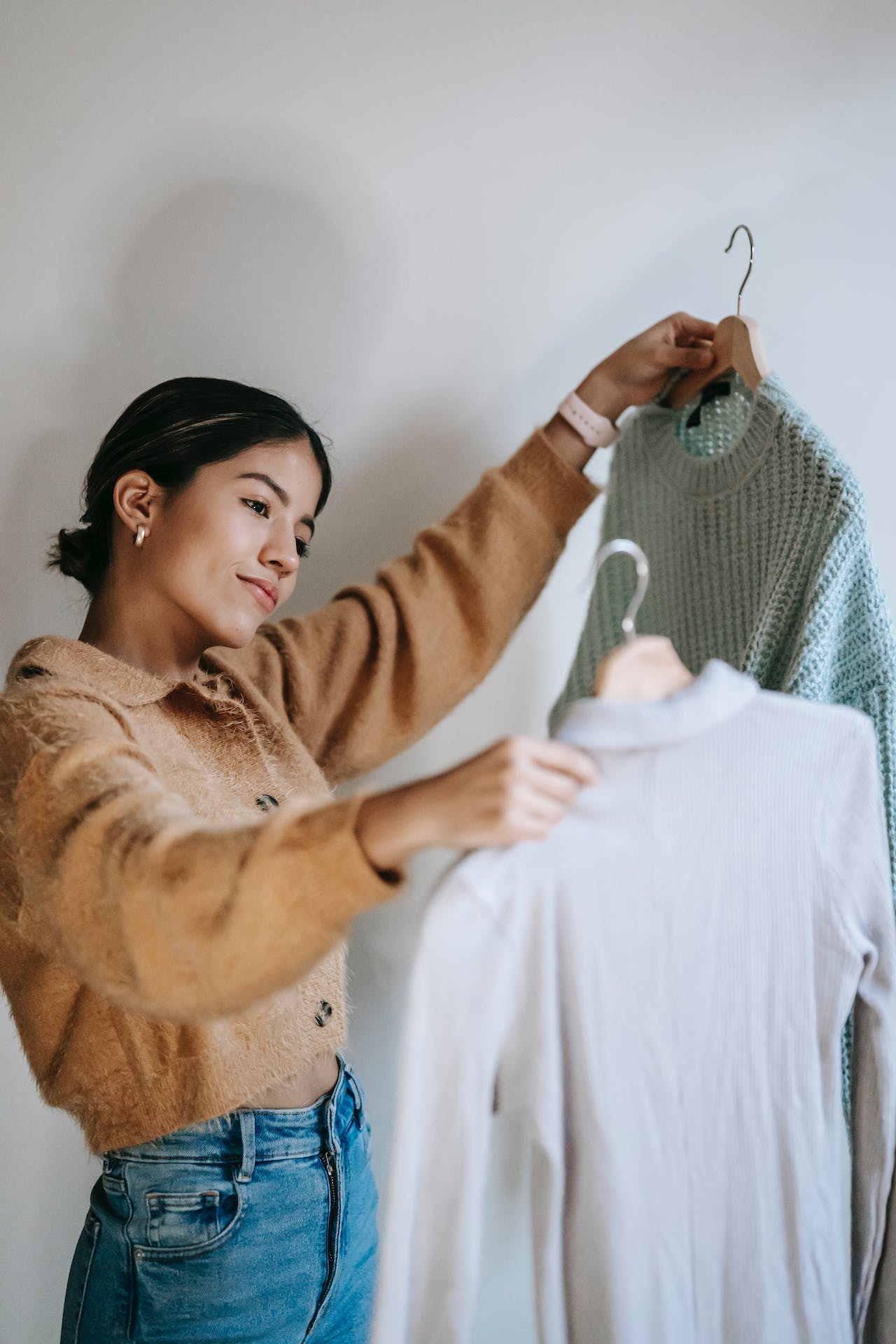 Happy young woman choosing pullovers on hangers