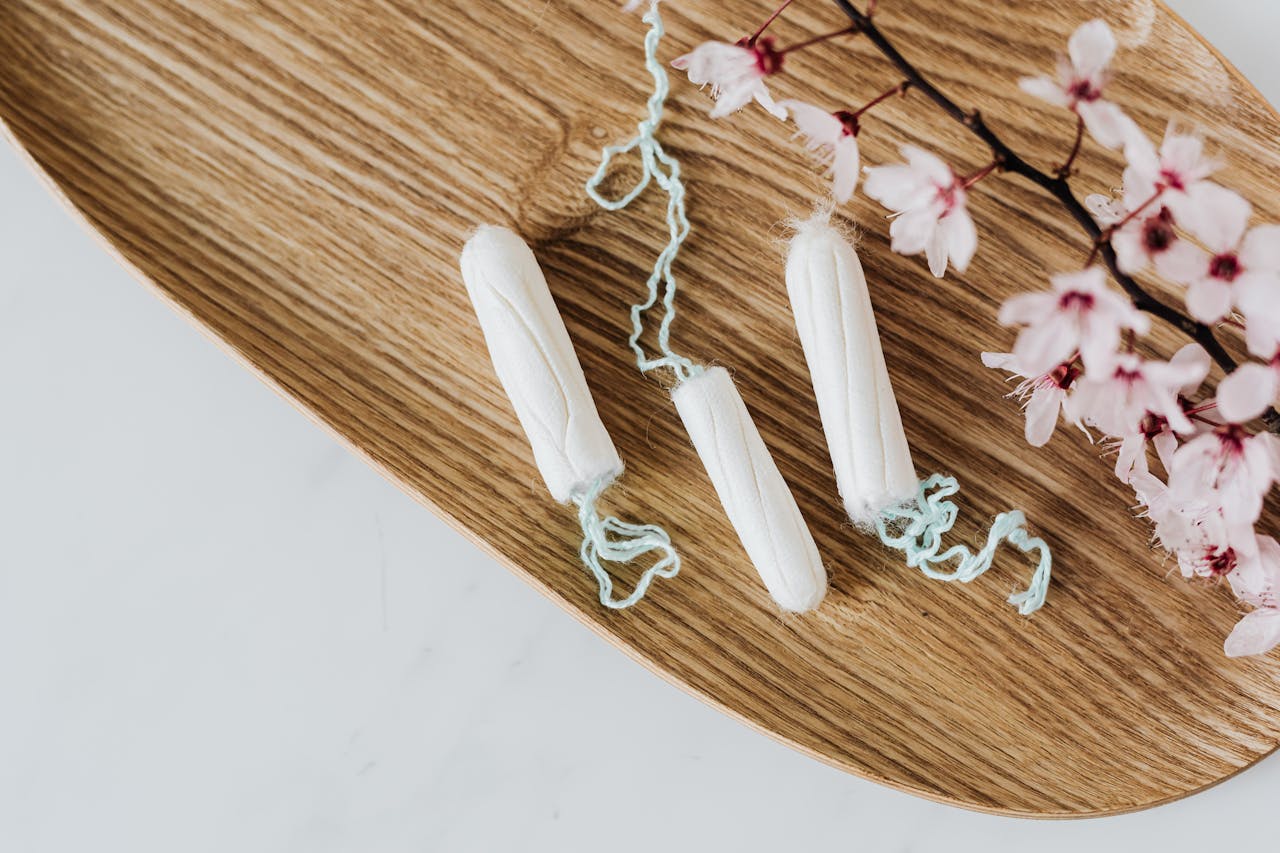 Cotton menstrual tampons and delicate flower branch on wooden board