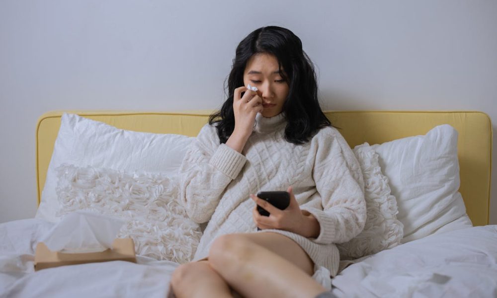 A Sad Woman Looking at her Cellphone While Sitting on a Bed