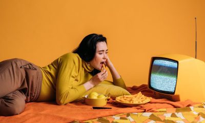 Woman in Yellow Long Sleeve Shirt Watching TV And Eating