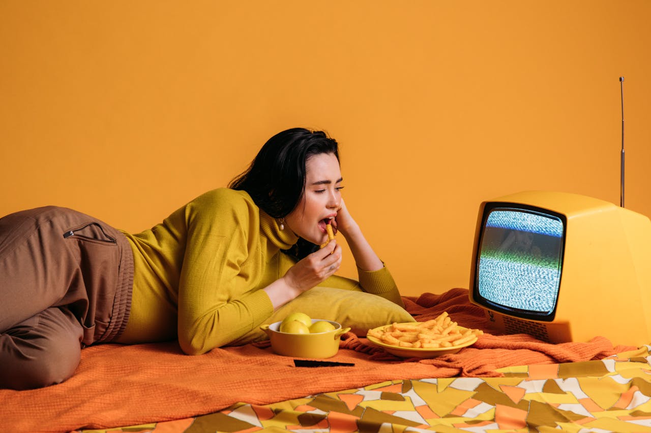 Woman in Yellow Long Sleeve Shirt Watching TV And Eating