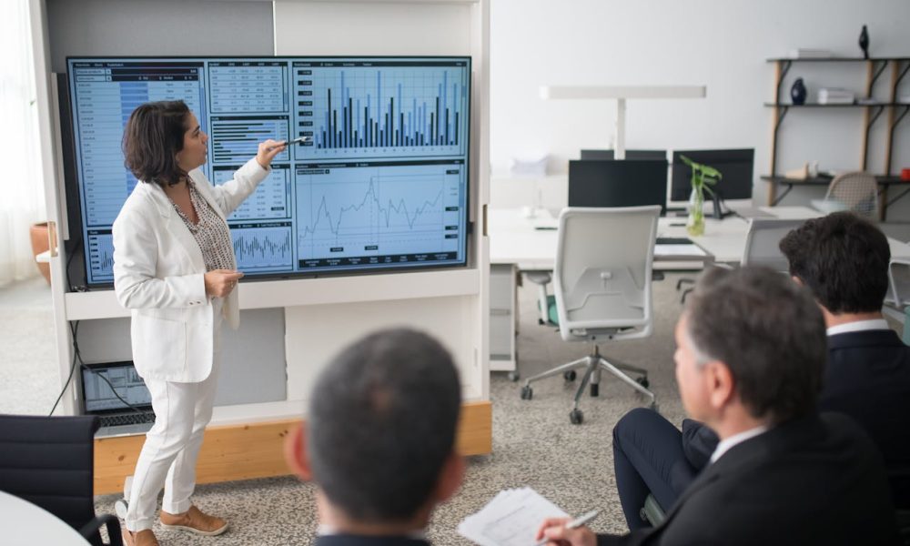 Woman in White Suit Discussing Stock Market Data To Her Colleagues